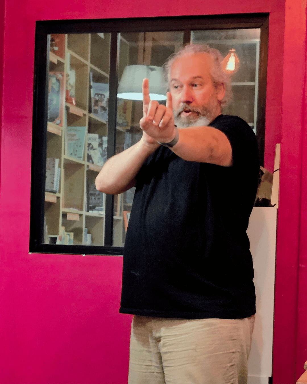 Stéphane est de face, il a un bras tendu devant lui, l'autre plié. Les index levés pour montrer des personnes qui font une file.